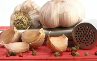 Головки чеснока, дольки и пресс на красной поверхности - ГИППОКРАТ