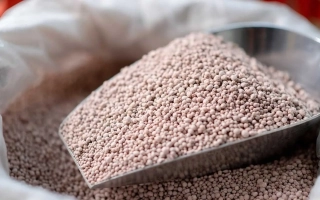 Коричневые гранулированные удобрения в металлической лопате на фоне мешка - НИТРОАМОФОСКА