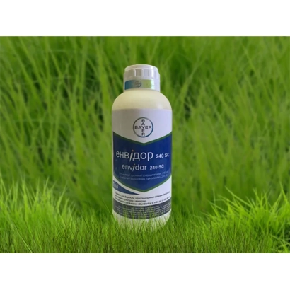 Бутылка с препаратом ЕЕНВИДОР 240 SC на фоне зеленой травы