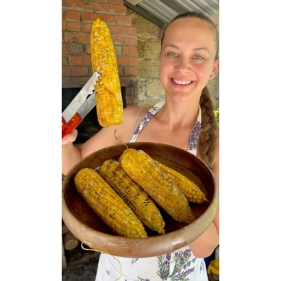 Женщина держит в руках кукурузу Усмишка в деревянной миске и с ножницами.