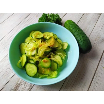 Салат з нарізаних огірків у синій мисці з цілим огірком та зеленню на дерев'яній поверхні - Пікантний
