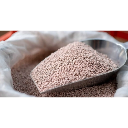 Brown granular fertilizers in a metal scoop against a bag background - NITROAMOFOSKA